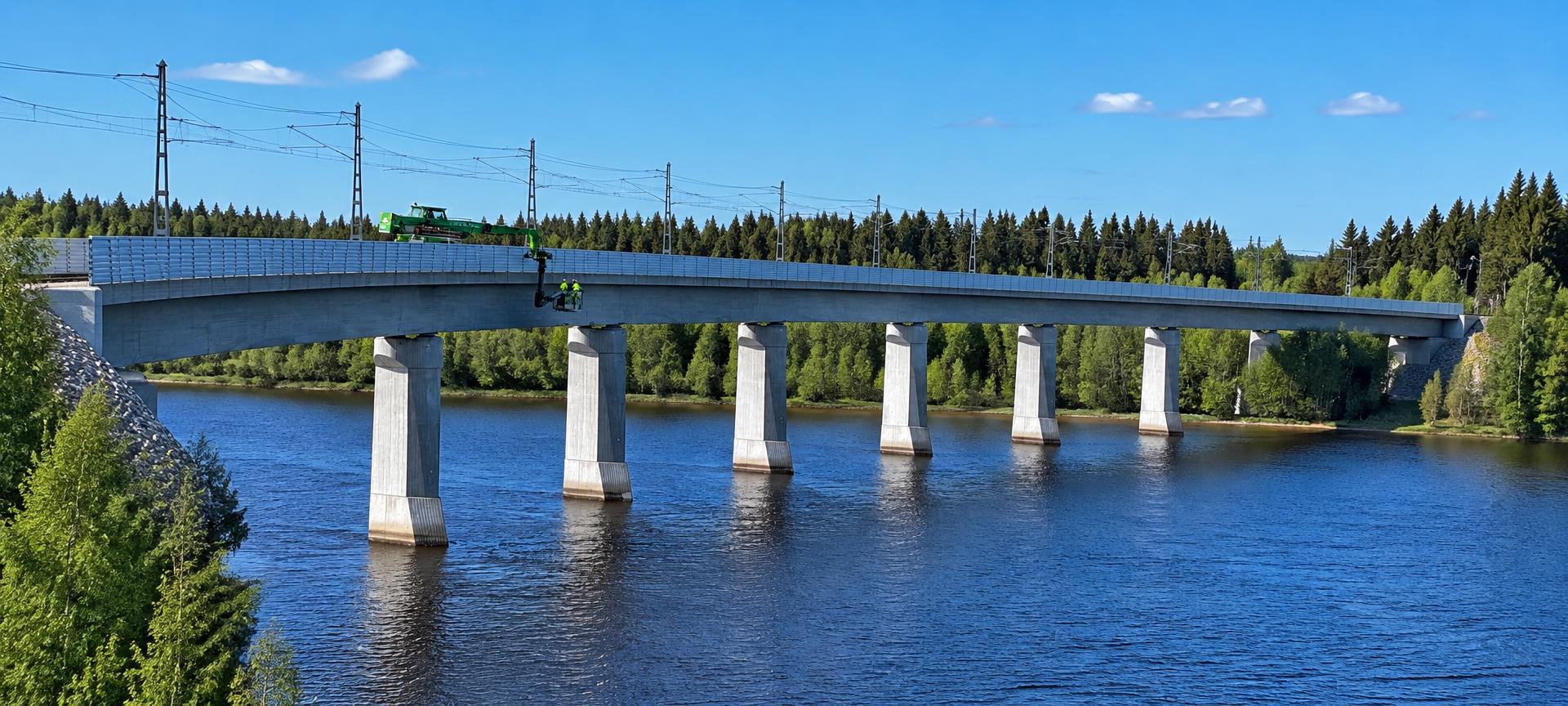 Besiktning av järnvägsbro med arbetslift och arbetare i varselkläder